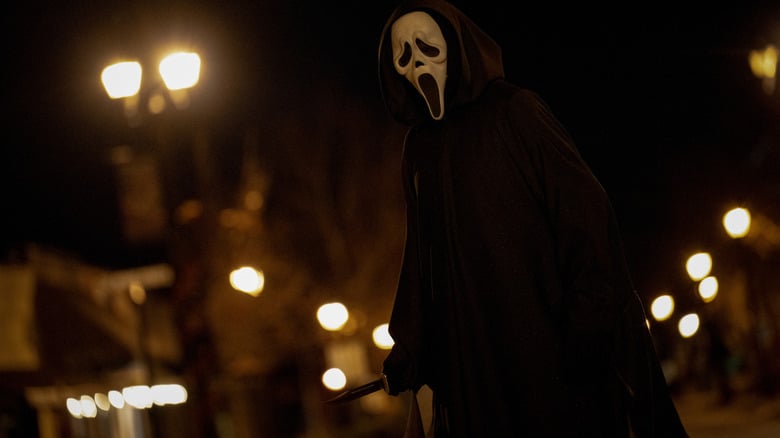 An unnamed actor as Ghostface standing in an empty street and brandishing a knife in Scream 7