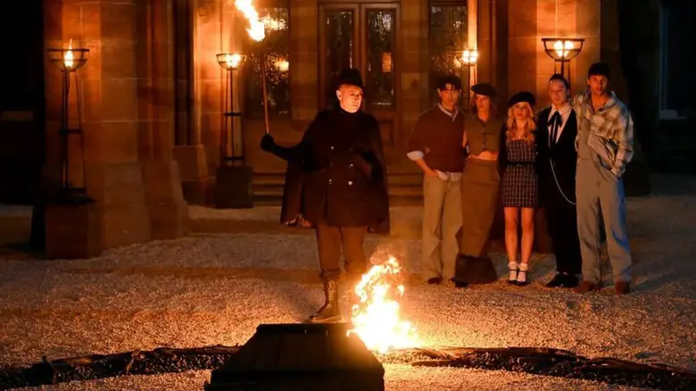 Alan holding a torch in front of Eric Maura Tara Johnny and Rob on The Traitors