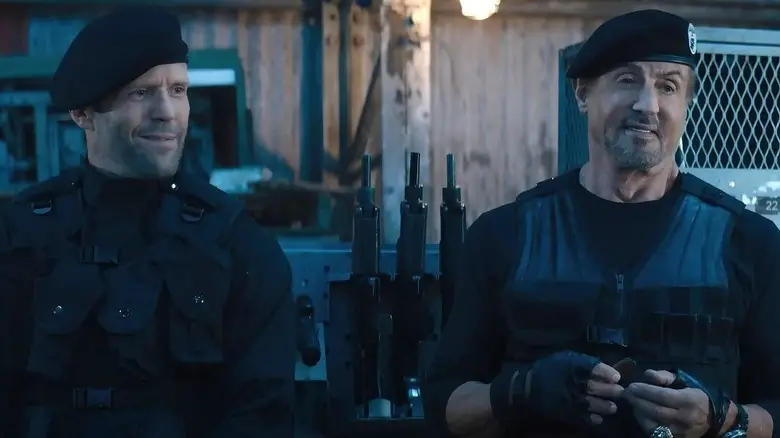 Jason Statham as Lee Christmas and Sylvester Stallone as Barney Ross in tactical gear standing in front of lockers in Expend4bles