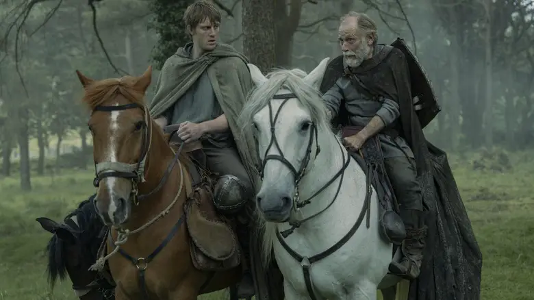 Peter Claffey as Dunk riding a horse alongside Danny Webb as Ser Arlan of Pennytree in the middle of a forest in A Knight of the Seven Kingdoms