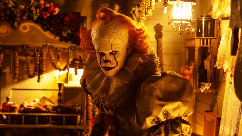 Bill Skarsgård's Pennywise stands looking menacing in a house in It: Welcome to Derry