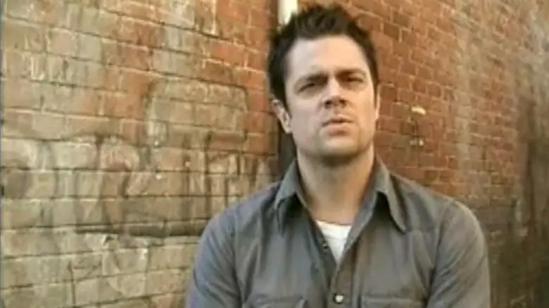 Johnny Knoxville stares into the camera while standing by a brick wall in Jackass