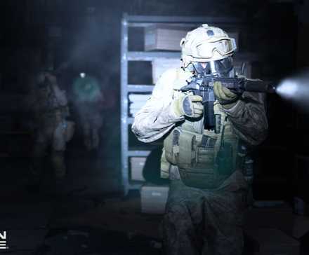 A soldier moves through a dark room, a flashlight attached to his gun