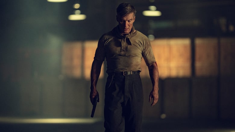 Cillian Murphy as Tommy Shelby covered in dirt and holding a gun in his hand as he walks through an empty warehouse in Peaky Blinders: The Immortal Man