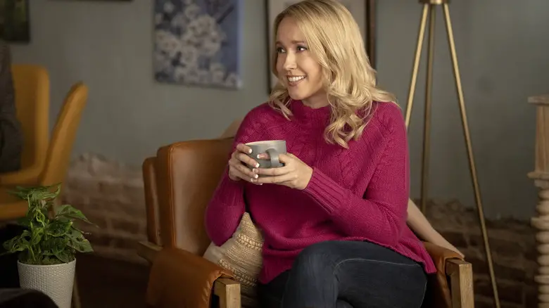 Anna Camp as Jessica Bowden sitting in a chair and drinking coffee in Scream 7