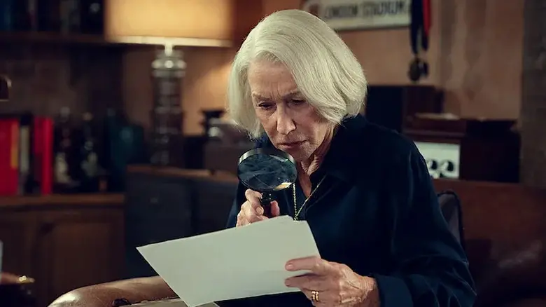 Elizabeth Best (Helen Mirren) examines a document with a magnifying glass in The Thursday Murder Club