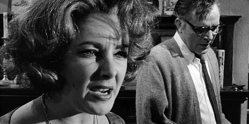 A close up of Elizabeth Taylor with Richard Burton in the background