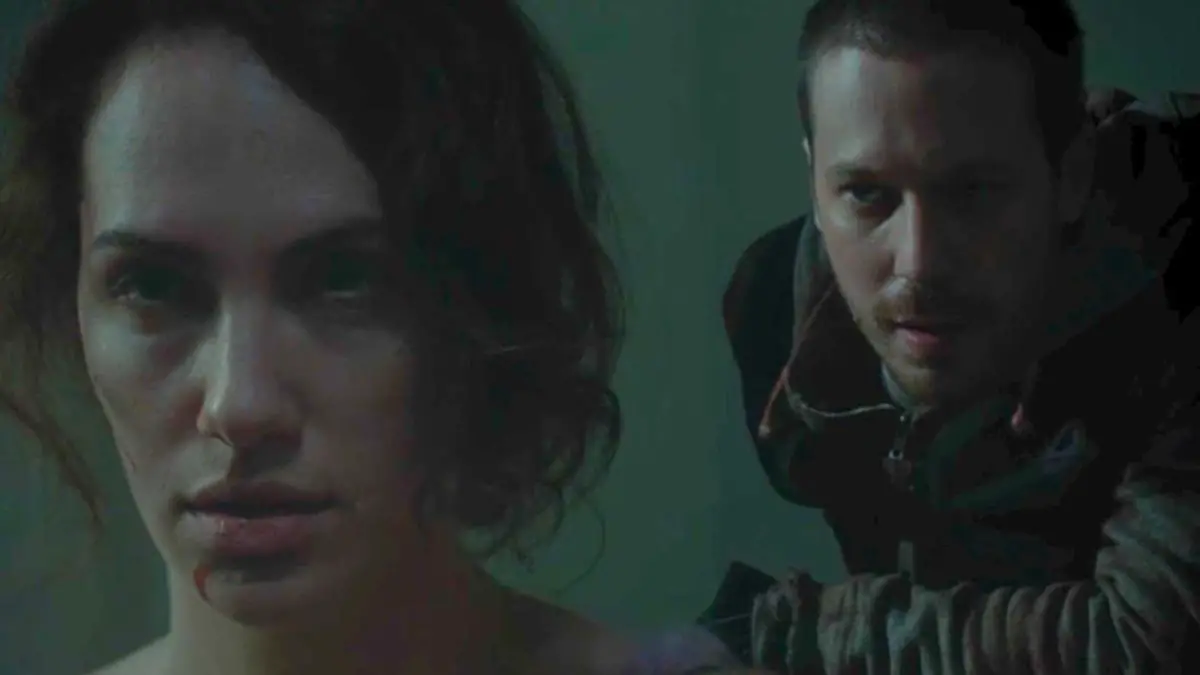 A man in a zipped up hoodie lures behind Maddie Young (Kate Siegel) who is bloodied and bruised.