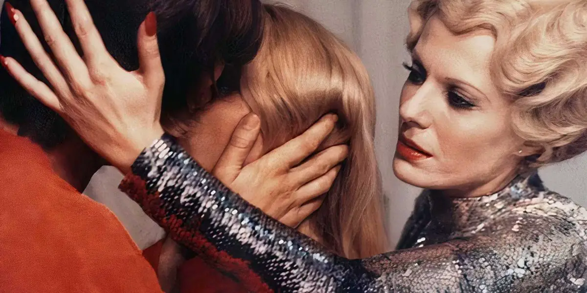 Delphine Seyrig in Daughters of Darkness holding a man's head while he kisses a woman.