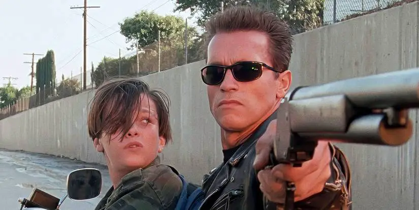 The T-800 aiming a rifle while John Connor sits in front of him in Terminator 2: Judgment Day